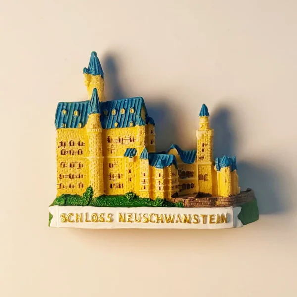 Front view of a detailed, hand-painted 3D Neuschwanstein Castle fridge magnet, showcasing its iconic yellow walls and blue turrets, with "SCHLOSS NEUSCHWANSTEIN" on the base.