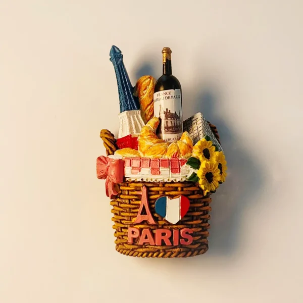 Front view of a detailed Paris picnic basket fridge magnet featuring the Eiffel Tower, wine, baguette, croissant, and sunflowers, with 'PARIS' text and French flag heart.