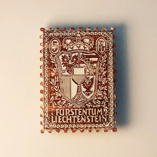 Front view of a 3D relief Liechtenstein national coat of arms stamp-shaped fridge magnet with vintage hand-painted details.