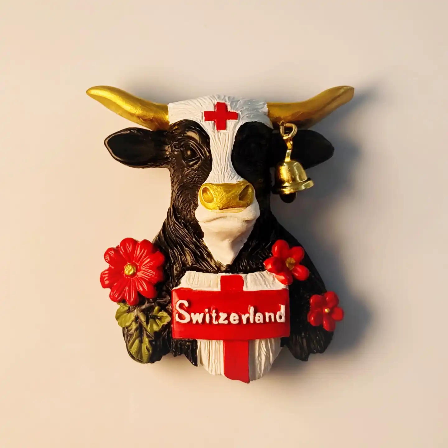 Front view of a hand-painted 3D Switzerland Alpine Bell Cow fridge magnet, featuring golden horns, a bell, and a "Switzerland" banner.
