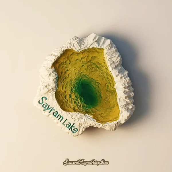 An angled view of the 3D relief Sayram Lake travel magnet highlighting the deep green center and textured white border.