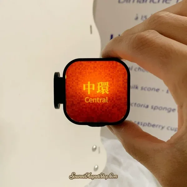 Hand holding lit Hong Kong Central MTR fridge magnet showing vibrant orange glow and gold Chinese station name
