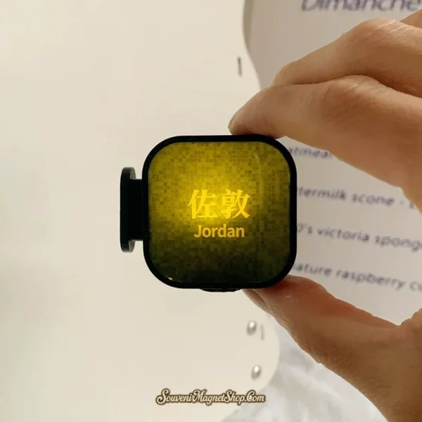 Hand holding lit Jordan MTR fridge magnet showing olive green glow and bright yellow Chinese station name