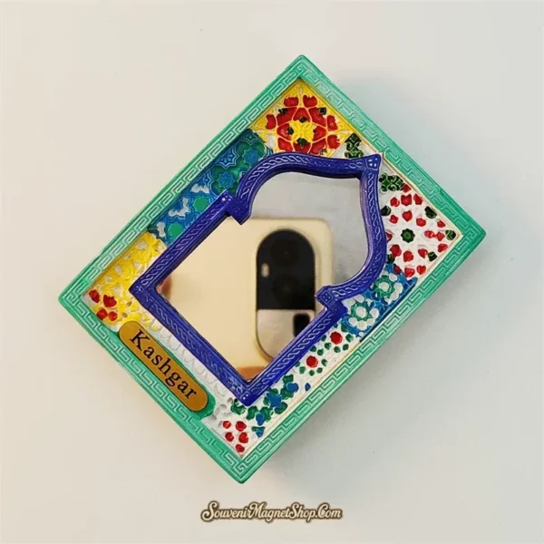 Angled view of Kashgar arch mirror fridge magnet showing teal green Greek key frame and colorful scattered floral background