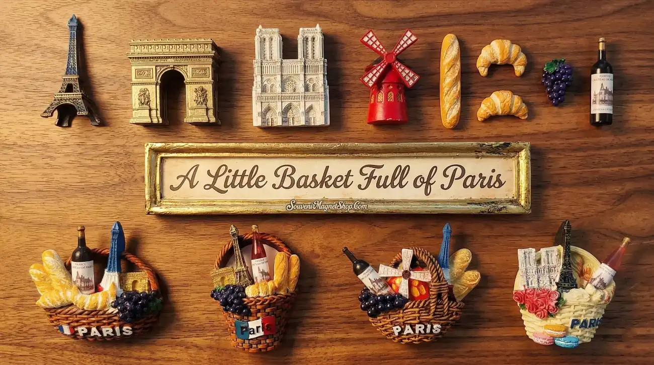 A knolling-style flat lay of Paris-themed 3D fridge magnets and miniature models on a warm wooden background, featuring the Eiffel Tower, Arc de Triomphe, Notre-Dame, Moulin Rouge, baguette, croissant, grapes, and wine bottle arranged above a retro "A Little Basket Full of Paris" souvenir magnet, with four wicker basket fridge magnets displayed below.