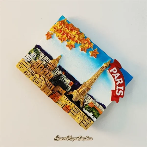 Angled view of Paris autumn fridge magnet showing 3D depth of orange maple leaves protruding from surface and gold Eiffel Tower