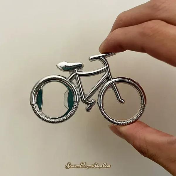 Hand holding silver bicycle fridge magnet showing bottle opener in rear wheel cutout