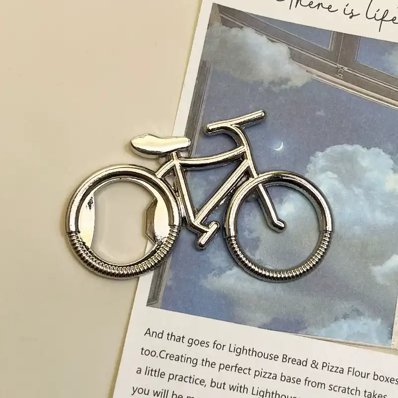 Silver retro bicycle bottle opener fridge magnet on dreamy sky art book, front angled view