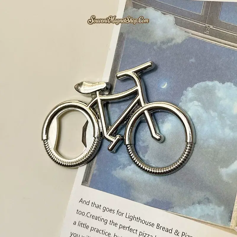 Silver retro bicycle bottle opener magnet on tilted art book showing chrome bicycle shape