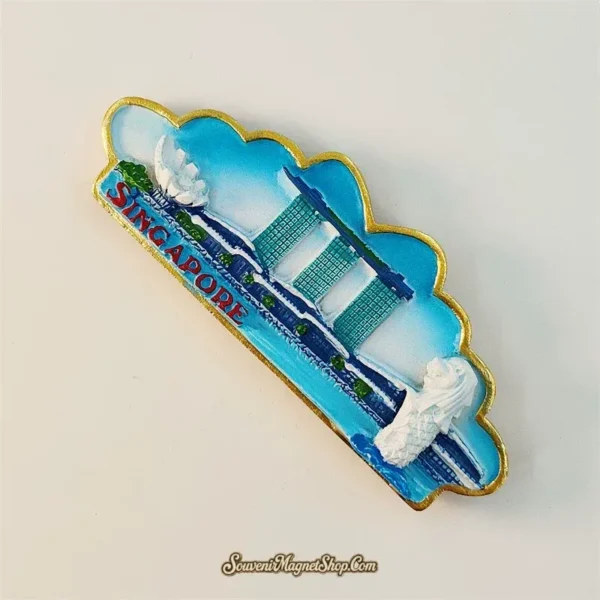 Angled view of Singapore cloud shape fridge magnet showing gold metallic border and 3D Marina Bay Sands and Merlion relief