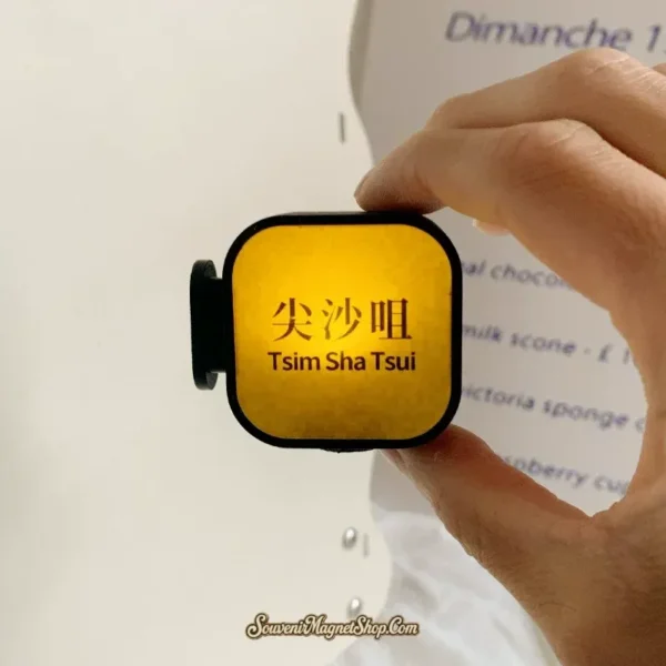 Hand holding glowing Tsim Sha Tsui MTR station fun fridge magnet showing lit yellow face