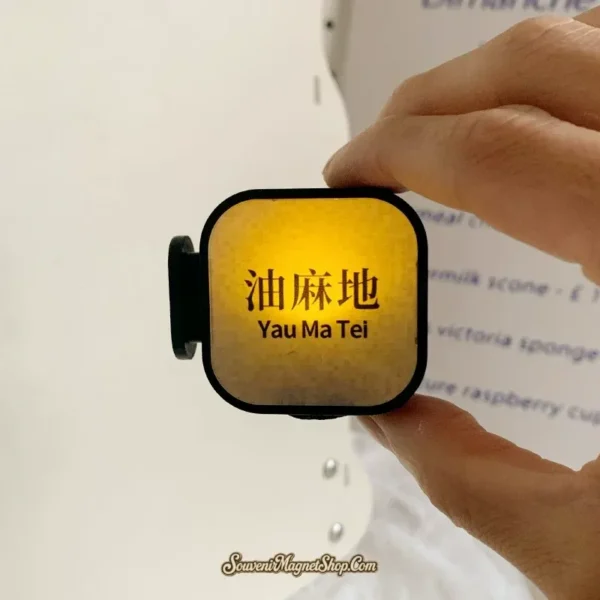 Hand holding lit Yau Ma Tei MTR fridge magnet showing strong golden amber glow and Chinese station name