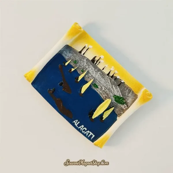 Angled view of hand-painted Alacati Turkey scroll magnet showing 3D relief windsurfers and coastline