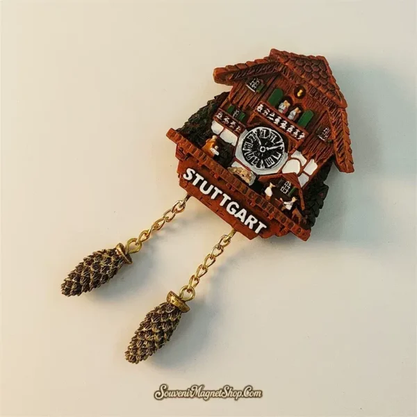 Stuttgart cuckoo clock souvenir fridge magnet angled left view revealing 3D depth of carved wooden chalet roof texture clock face and dangling gold chain pine cone weights