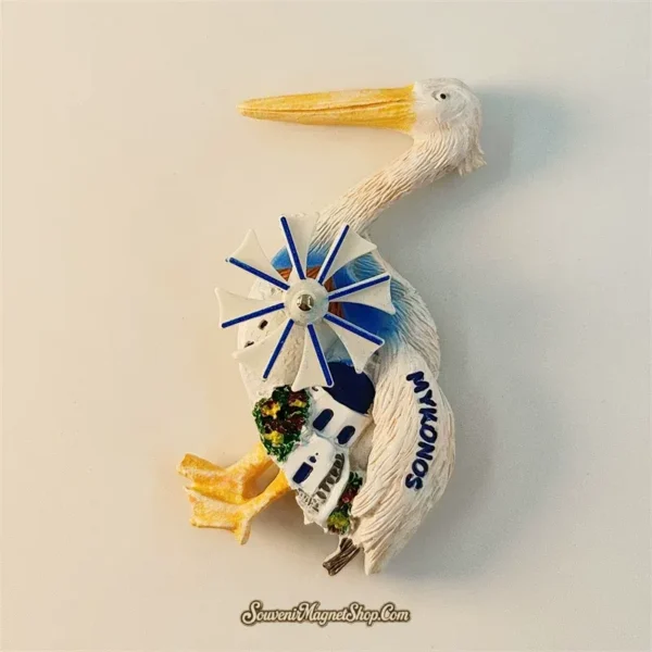 Mykonos souvenir fridge magnet angled right view revealing 3D depth of white pelican body yellow beak blue windmill spokes metal hub and Cycladic architecture detail