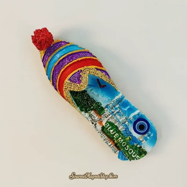 Angle view of the Istanbul Blue Mosque Turkish slipper souvenir magnet showing the curled toe, red pom-pom, and striped textile-pattern 3D body