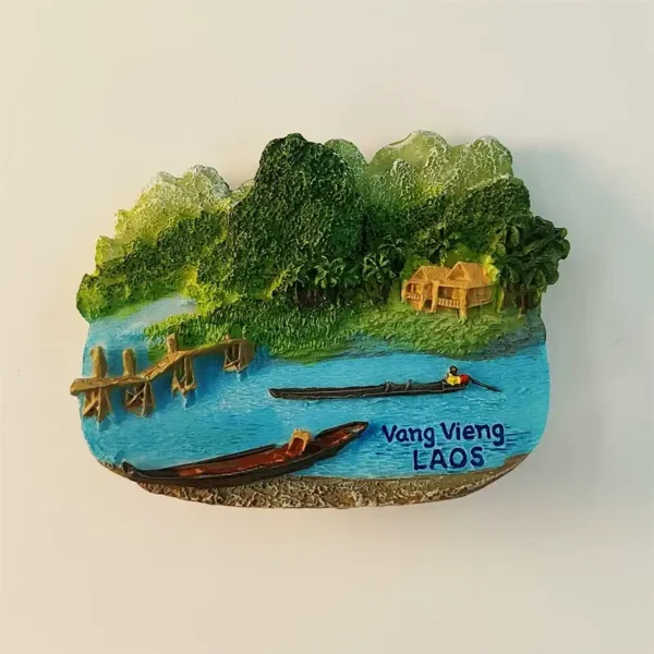 Laos Vang Vieng fridge magnet front view showing 3D Nam Song River scene with two wooden long-tail boats bamboo pier golden stilt house lush karst mountains and Vang Vieng LAOS blue text