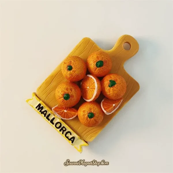 Spain Mallorca souvenir fridge magnet angled left view showing 3D depth of wooden cutting board shape with pile of hand-painted oranges and yellow MALLORCA ribbon
