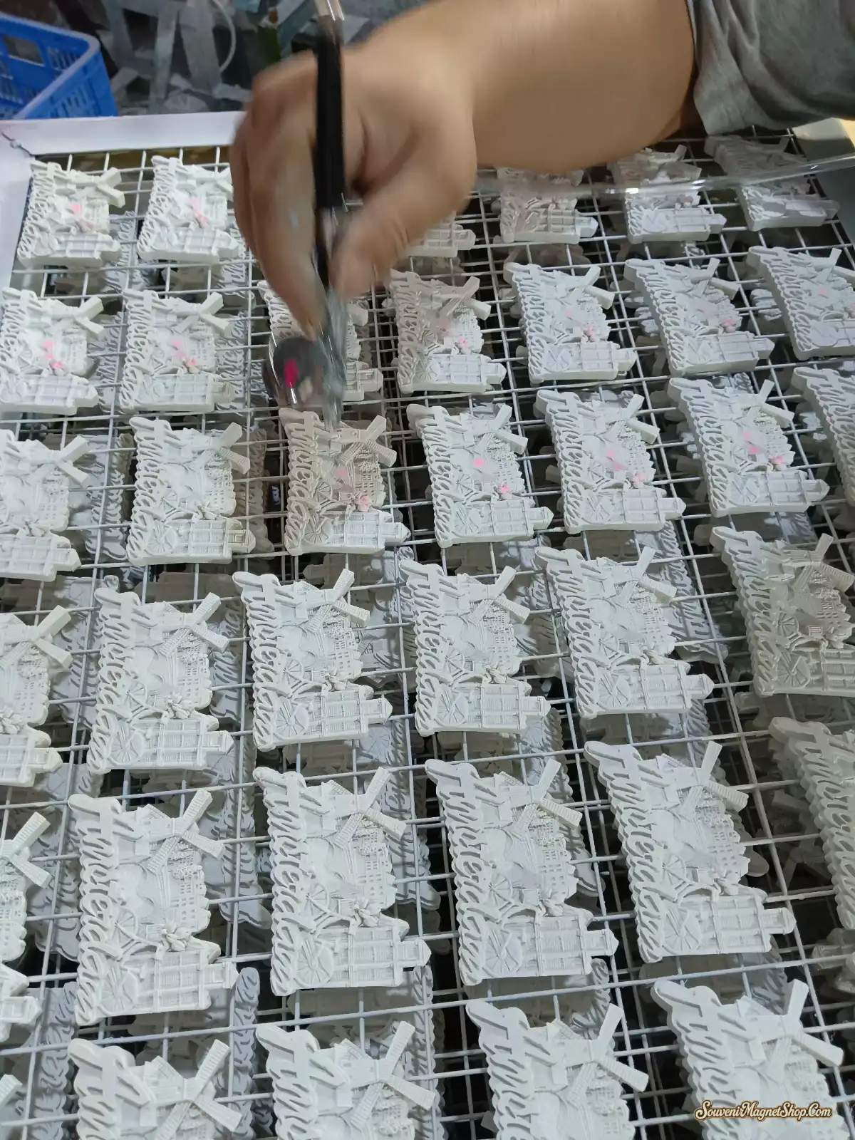 Hand-detailing white resin windmill souvenir magnets with pink-accent brushwork — the difference between a souvenir and a sticker, finished one piece at a time.