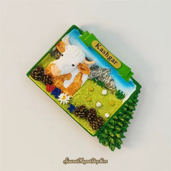 Angled view of Kashgar souvenir magnet showing 3D relief cow, meadow, pine cones and edelweiss