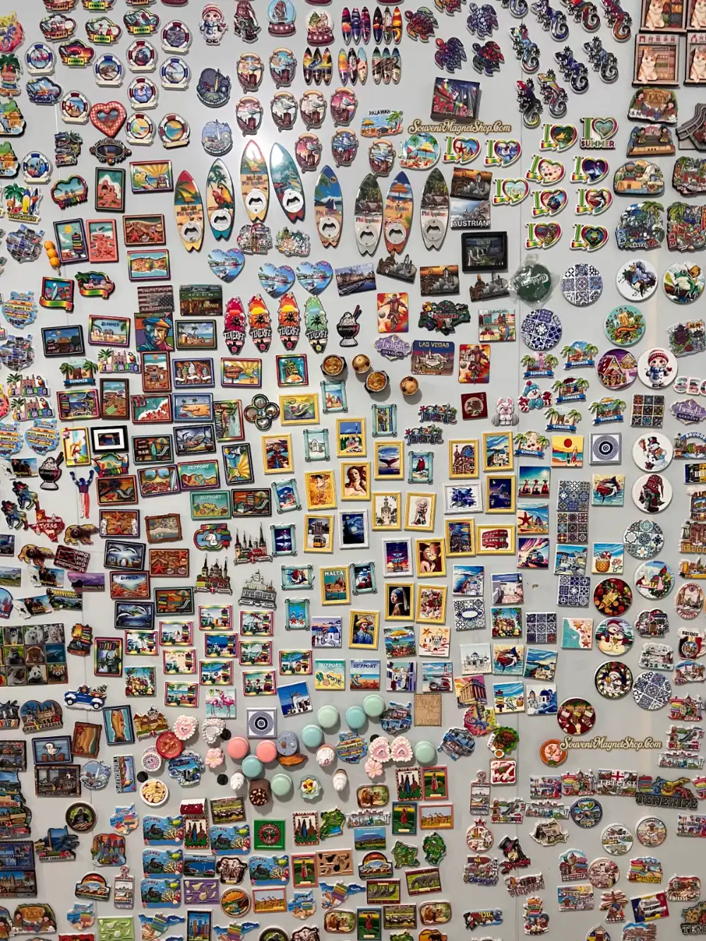 Our finished-products showcase wall — over 700 original souvenir fridge magnet designs spanning 80+ countries, from Tenerife and Malta to Las Vegas and Bruges.