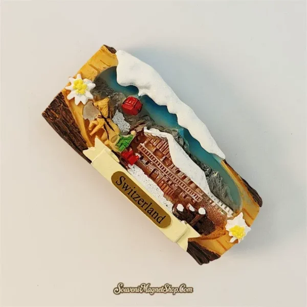 Angled view of Swiss Jungfrau souvenir magnet revealing 3D depth of snowy peaks, wooden chalet and red cableway above an alpine valley scene
