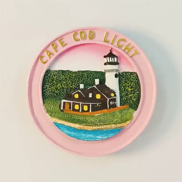 USA Cape Cod Lighthouse fridge magnet front view with hand-painted white light tower, brown keeper's cottage, green hedges and blue Atlantic shoreline in pink round frame