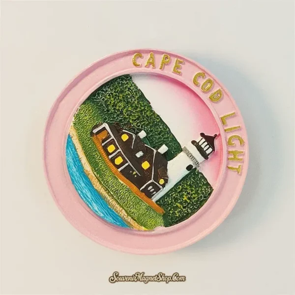 Cape Cod Lighthouse souvenir magnet angled view highlighting 3D hand-painted lighthouse, cottage and coastal scene on pink circular frame