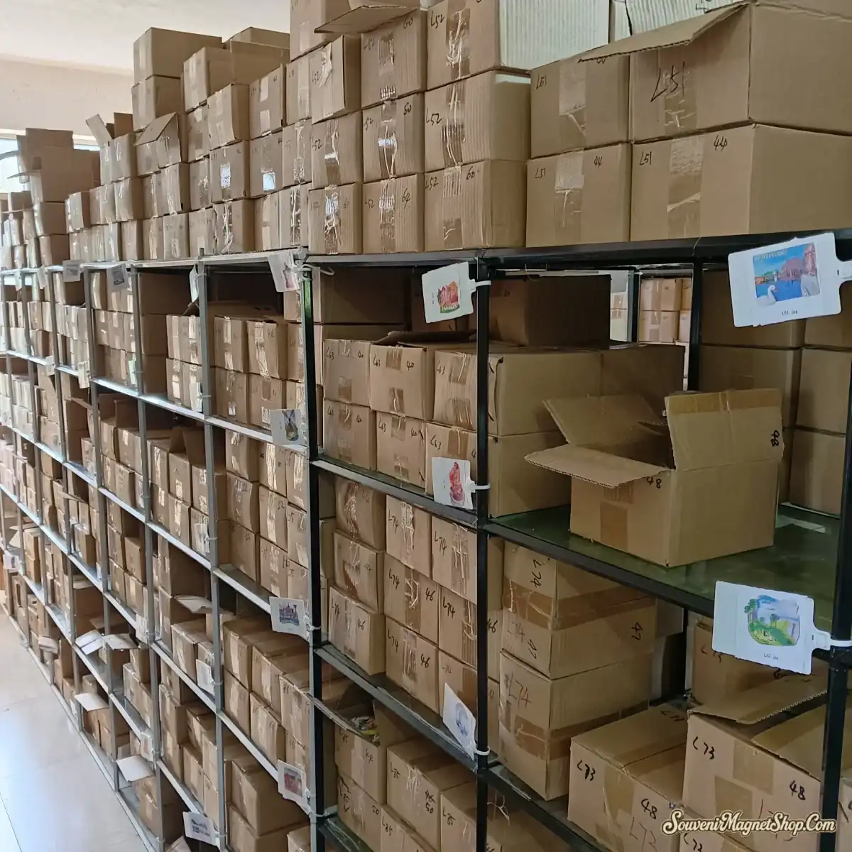 Our in-house warehouse — organized SKU shelving with a product sample card on every row, enabling 1–3 business-day order fulfillment to 77 countries.