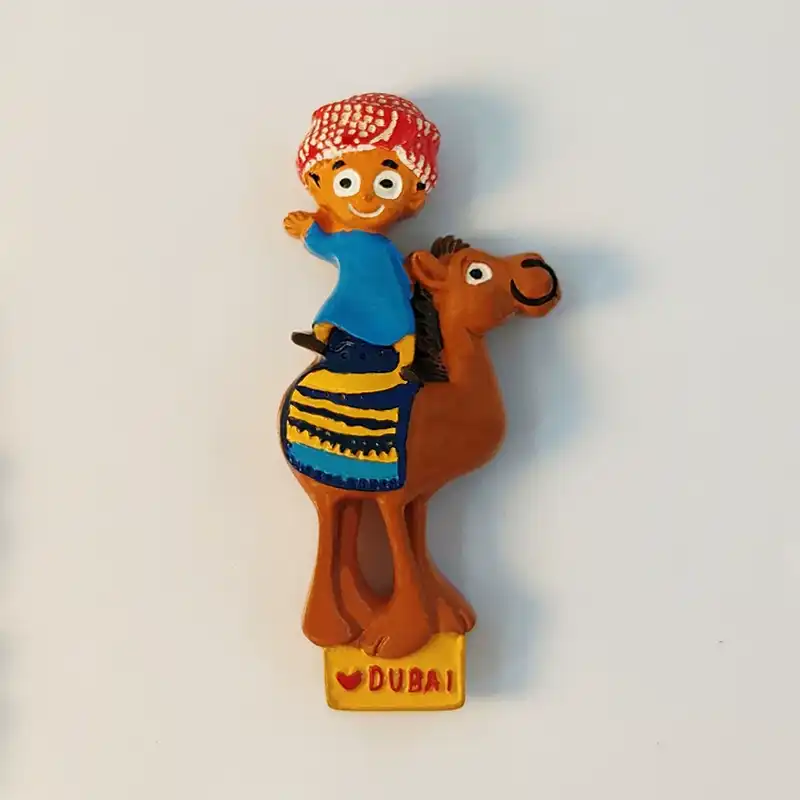 dubai-boy-riding-camel-fridge-magnet-front Dubai fridge magnet of cartoon boy riding a camel in red cap and blue robe, front view