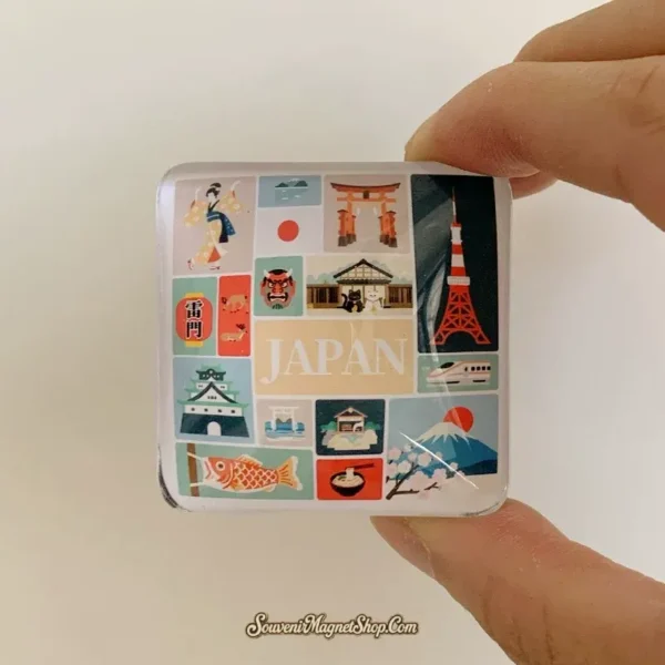 Hand holding a glossy domed Japan crystal glass souvenir fridge magnet showing the colorful icon collage and JAPAN lettering