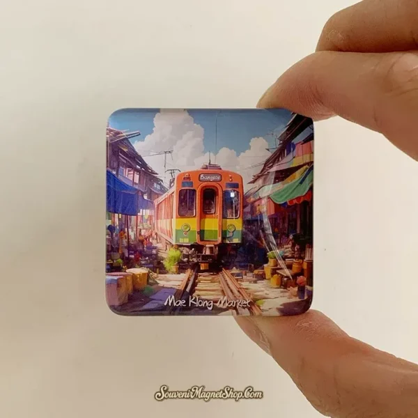 Hand holding Maeklong Market glass magnet showing the rainbow Bangkok train scene