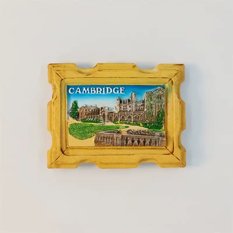 Front view of a Cambridge University fridge magnet with a carved gold frame and hand-painted college buildings under a blue sky