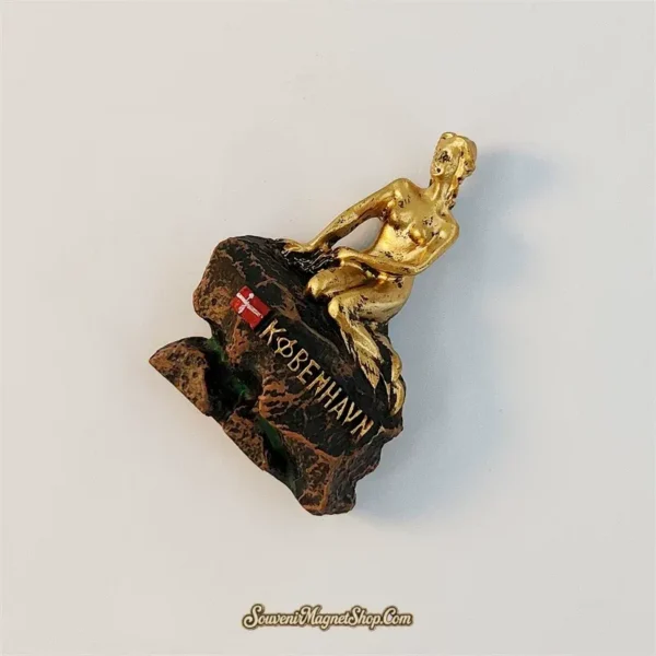 Side angle of the Copenhagen Little Mermaid souvenir magnet showing the gold figure reclining on a hand-painted bronze rock
