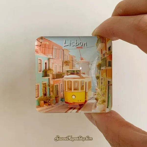 Hand holding the Lisbon yellow tram souvenir magnet showing its glossy domed glass and square size