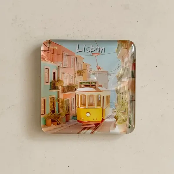 Front view of glass Lisbon fridge magnet with yellow tram on a pastel street and Lisbon lettering
