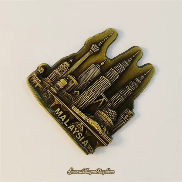 Angled Kuala Lumpur souvenir magnet showing the Petronas Towers and KL Tower skyline in raised antique-gold metal detail