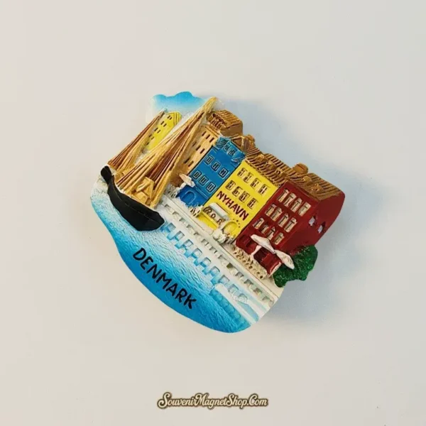 Angled view of the Copenhagen Nyhavn souvenir magnet highlighting the 3D relief of gabled harbour houses and a moored wooden sailboat.