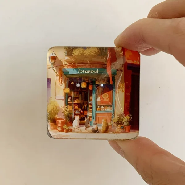 Hand holding the Istanbul cat shop glass fridge magnet showing its small square size