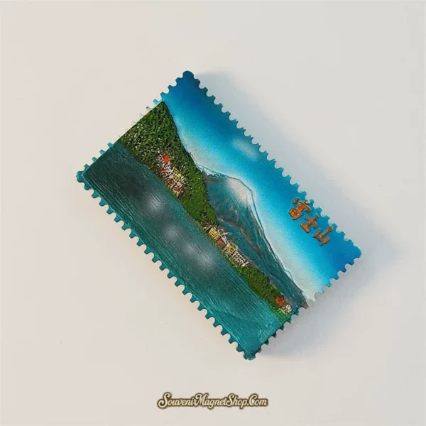 Angled view of the 3D Mount Fuji stamp fridge magnet with perforated edges and gold Japanese lettering