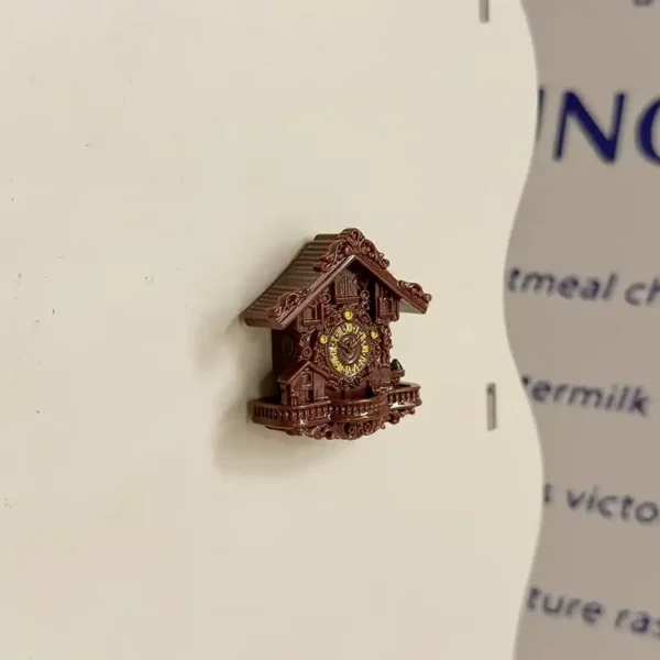 Brown cuckoo clock fridge magnet on a white fridge door beside a printed recipe card