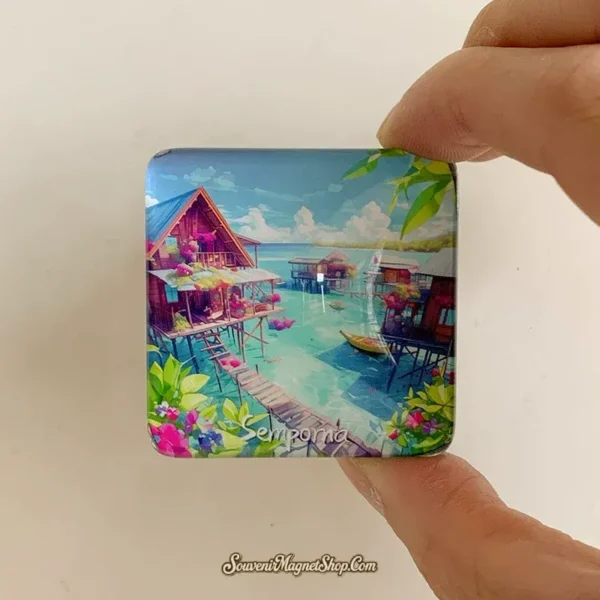 Hand holding the small glass-domed Semporna magnet showing the glossy stilt village scene