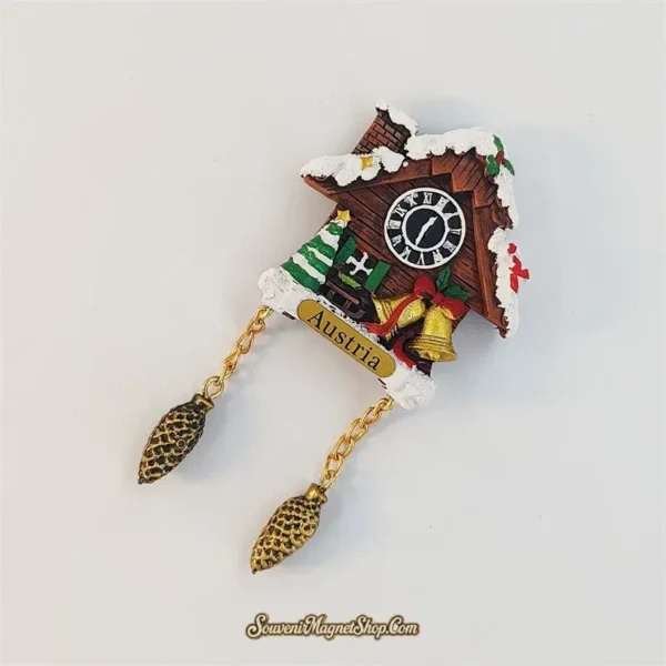 Angled view of the Austria cuckoo clock fridge magnet showing the snow-covered roof, Roman numeral clock and gold chains.