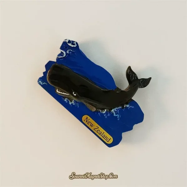 Sperm whale fridge magnet tilted clockwise, showing the broad head, small flipper and upturned tail against blue water.