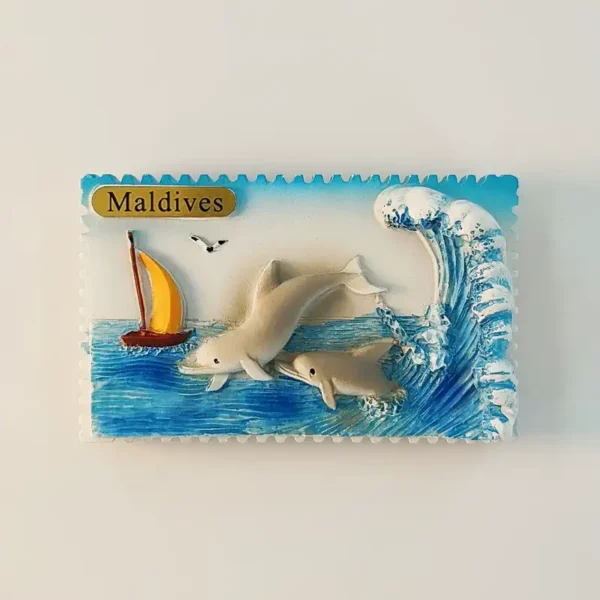 Maldives fridge magnet with two dolphins, a yellow sailboat, blue ocean, and a curling wave in a stamp-edged frame.