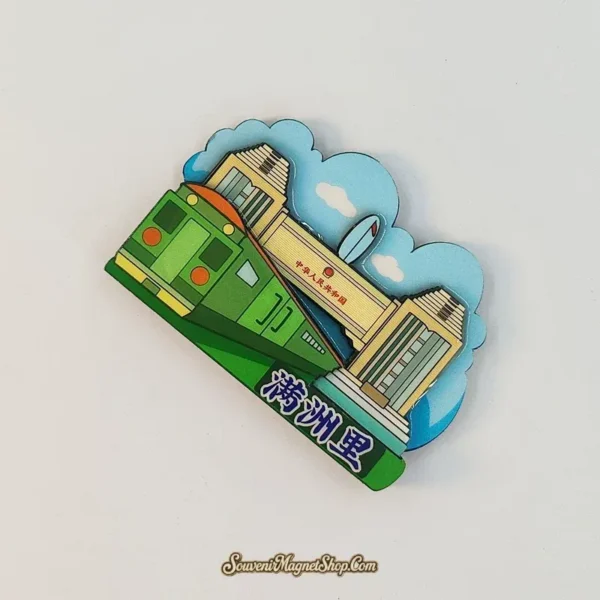 Angled Manzhouli fridge magnet showing the green train crossing in front of the pale border gate and blue cloud backdrop.