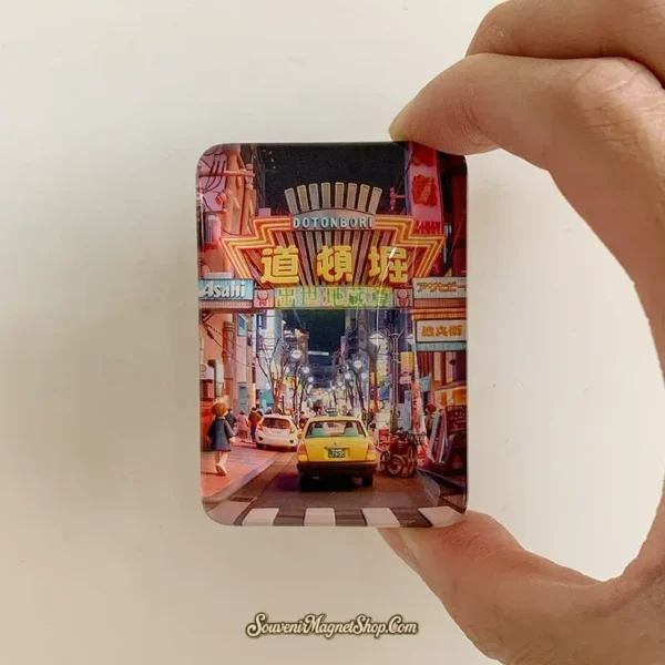Hand-held view of the Osaka Dotonbori glass fridge magnet showing its rounded rectangular shape and neon night street artwork.