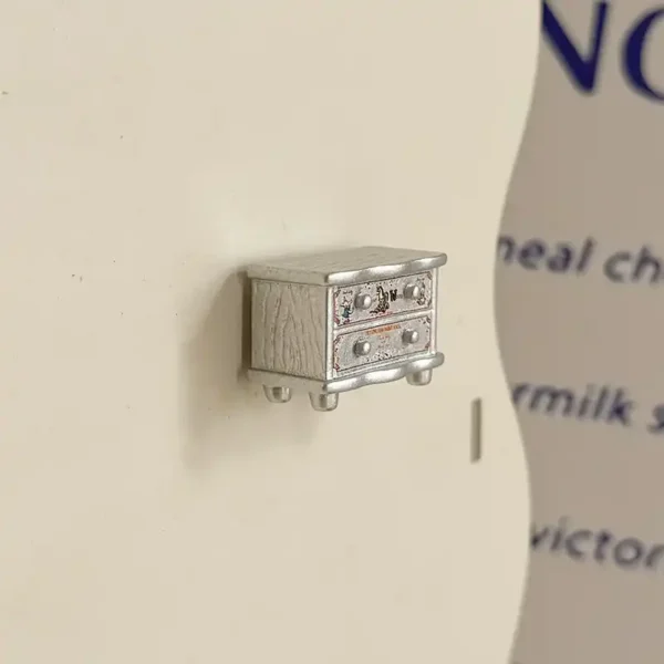 Cute silver bedside cabinet fridge magnet with two drawers, round knobs, short feet, and textured side panels.