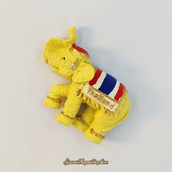 Angled view of the golden Thailand elephant fridge magnet showing its lifted leg, textured body and striped saddlecloth.