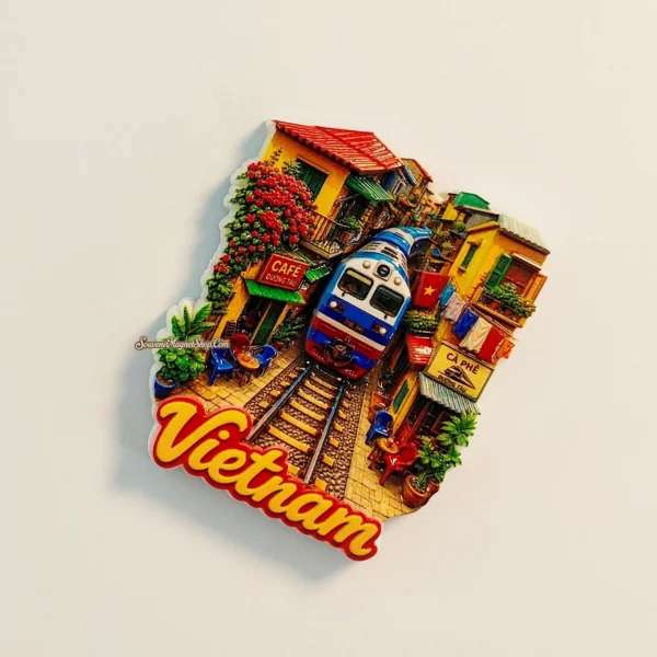 Hanoi Train Street fridge magnet tilted clockwise, showing raised train and café details, red flowers and Vietnam lettering.